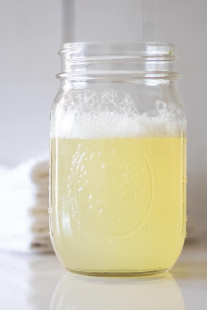 homemade bubble bath in a 1 qt mason jar on white marble with a small stack of decorative white towels