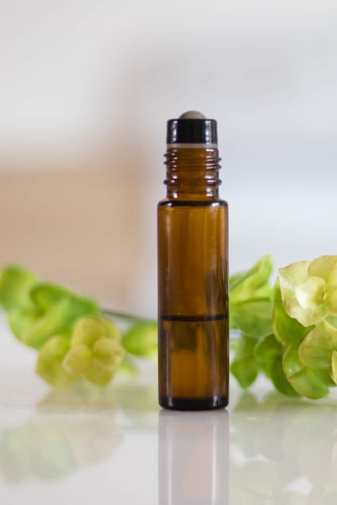 essential oil roller bottle blend with green leaves on a white background