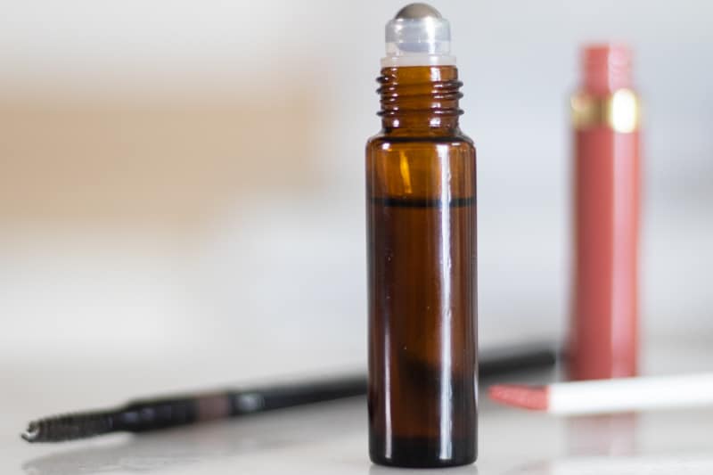 essential oils for eyebrow growth roller bottle with pink lip gloss in background