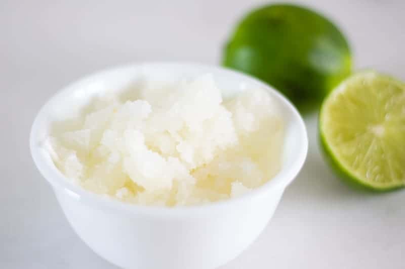 Sumer body scrub in white bowl with key limes on white marble.