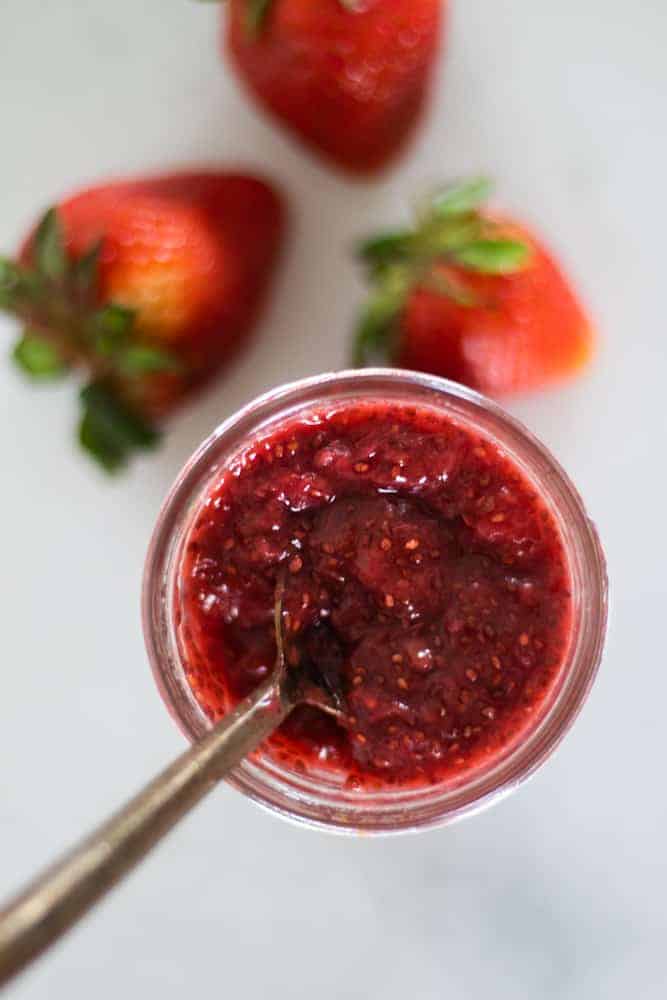 homemade strawberry jam in mason jar with gold spoon in it