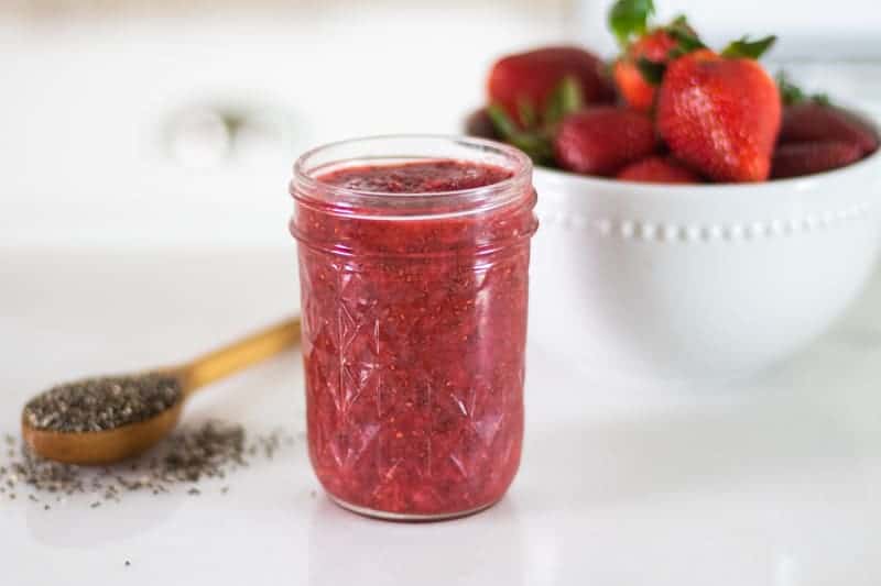 strawberry jam in mason jar with chia seeds and strawberries in background