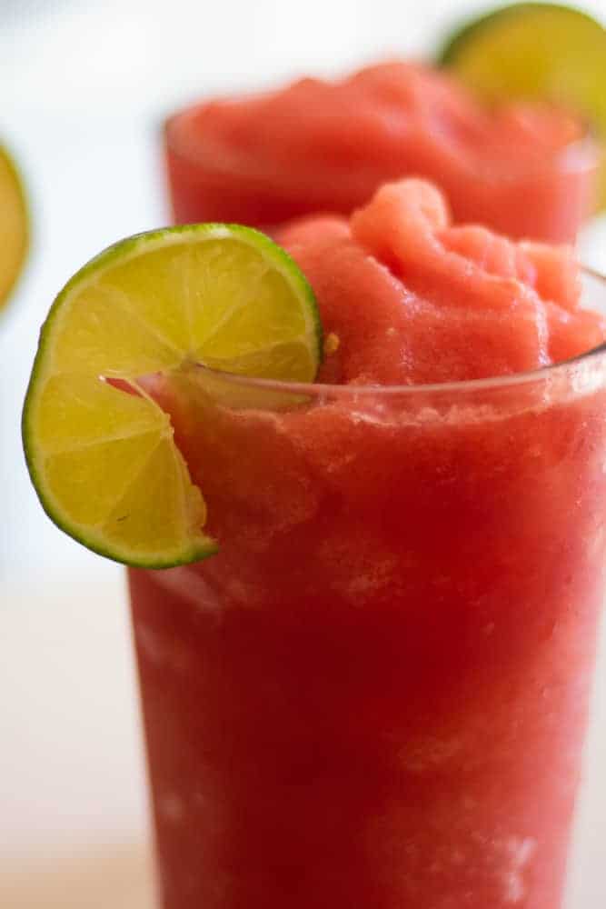 A watermelon slushie with lime slice close up on white background.