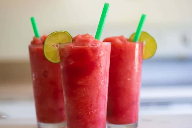 three red watermelon slushies with lime slices and green straws