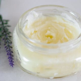 homemade burn salve in clear jar with lavender sprigs on white marble