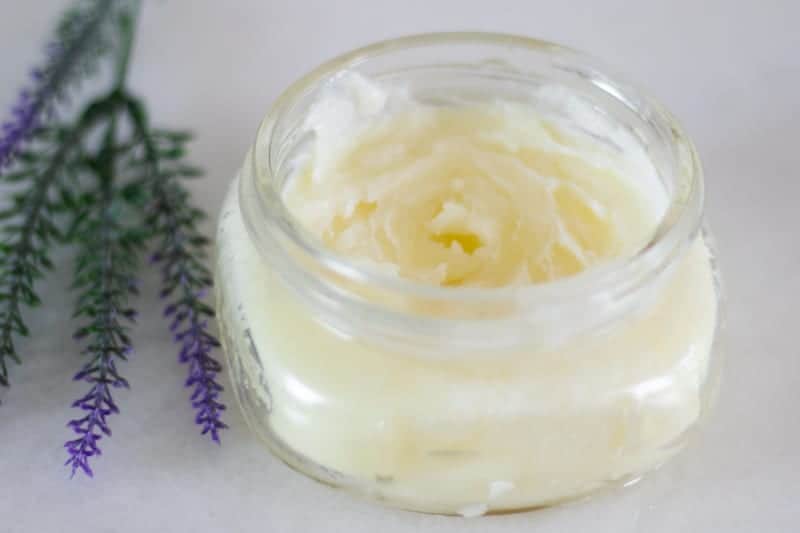 homemade burn salve in clear jar with lavender sprigs on white marble