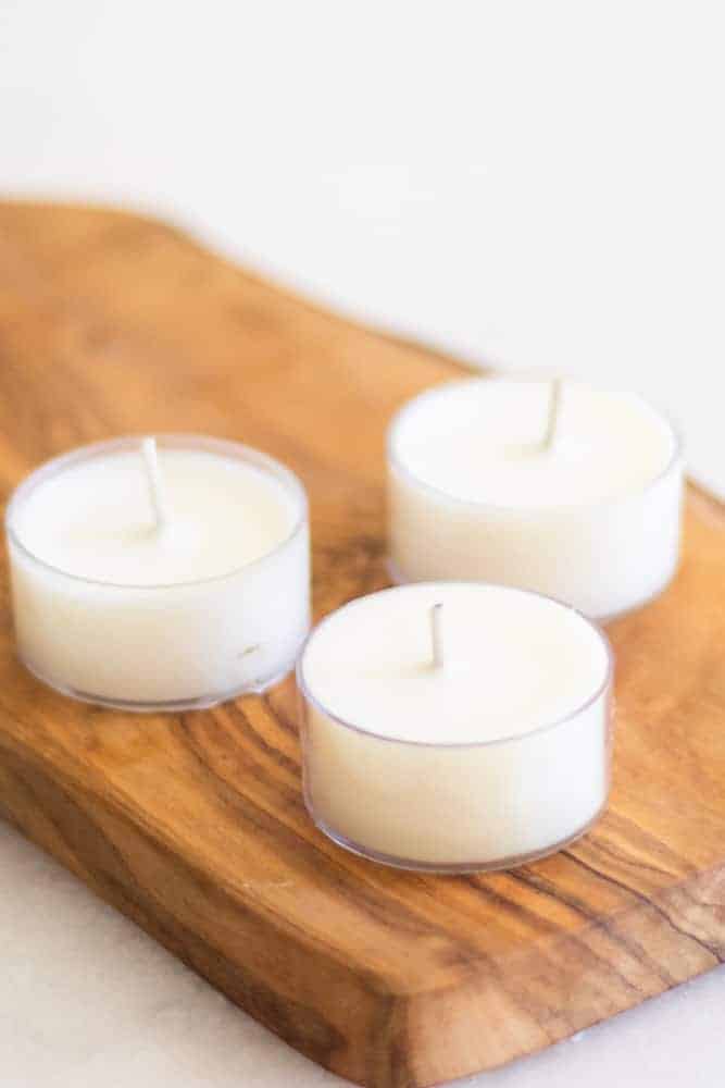 three white tea light candles on wooden cutting board.
