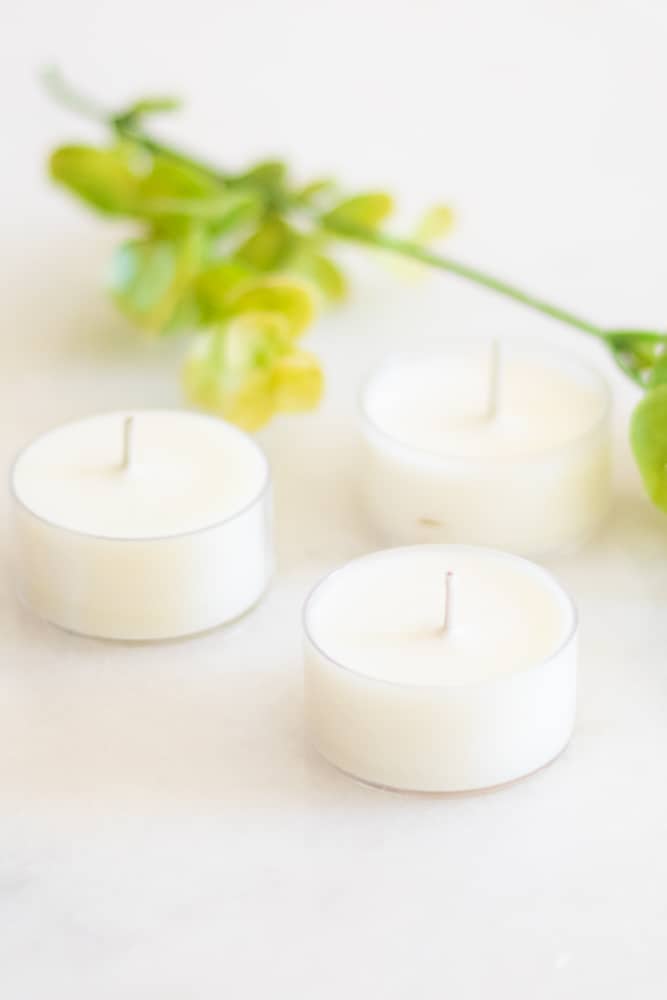 Homemade white citronella candles on white marble with greenery in background.