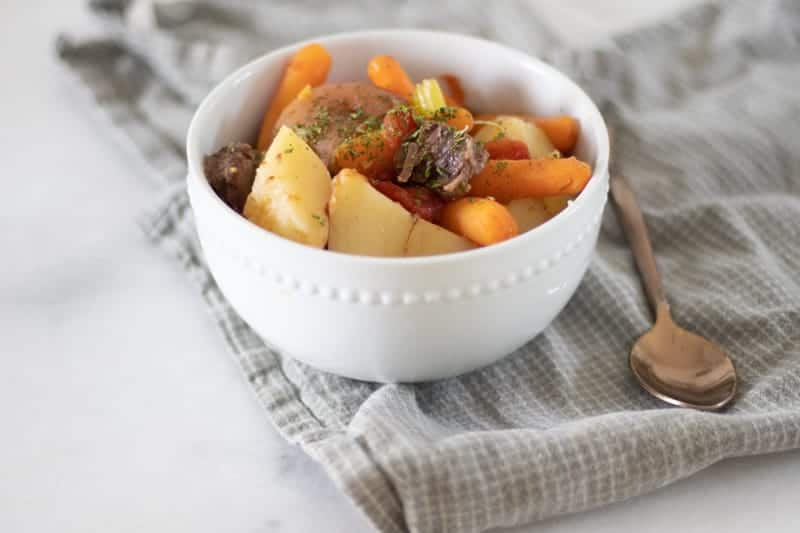 beef shank stew in white bowl on folded towel and white marble countertop