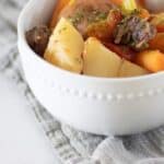 Bowl of beef shank stew in white bowl on gray towel.