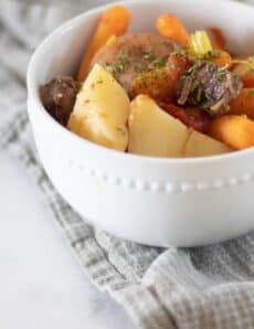 Bowl of beef shank stew in white bowl on gray towel.