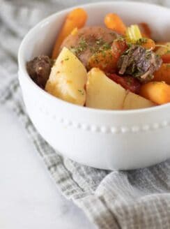 Bowl of beef shank stew in white bowl on gray towel.