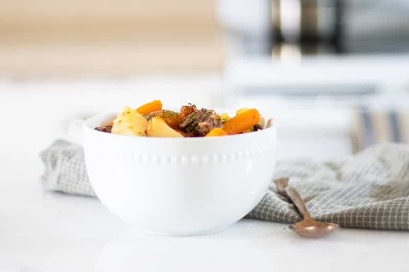 white bowl of beef shank stew on marble countertop with a green and gray towel and gold spoon in background