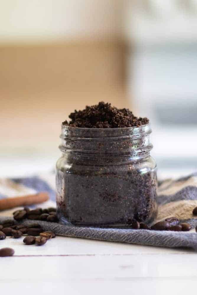 diy coffee scrub in mason jar with coffee beans and wooden spoon on white shiplap.