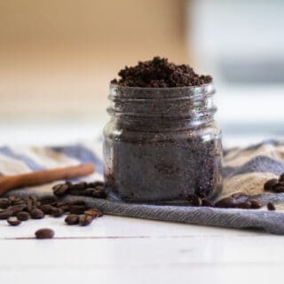 Organic coffee scrub in mason jar with wooden measuring spoon coffee beans and a blue and white striped towel.