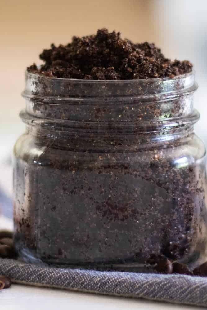 Body scrub with ground coffee and sugar on a blue and white towel.
