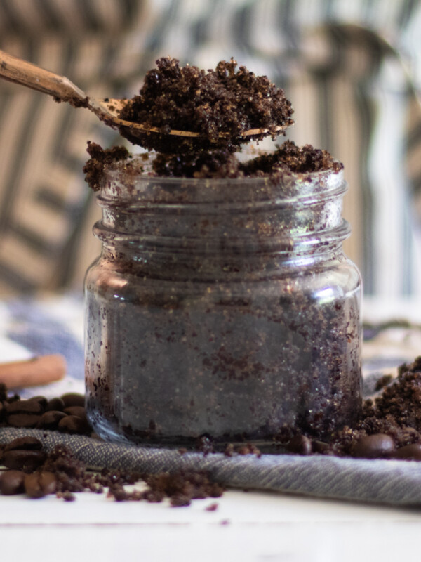 scooping out some homemade coffee scrub with a gold spoon to apply to the face.