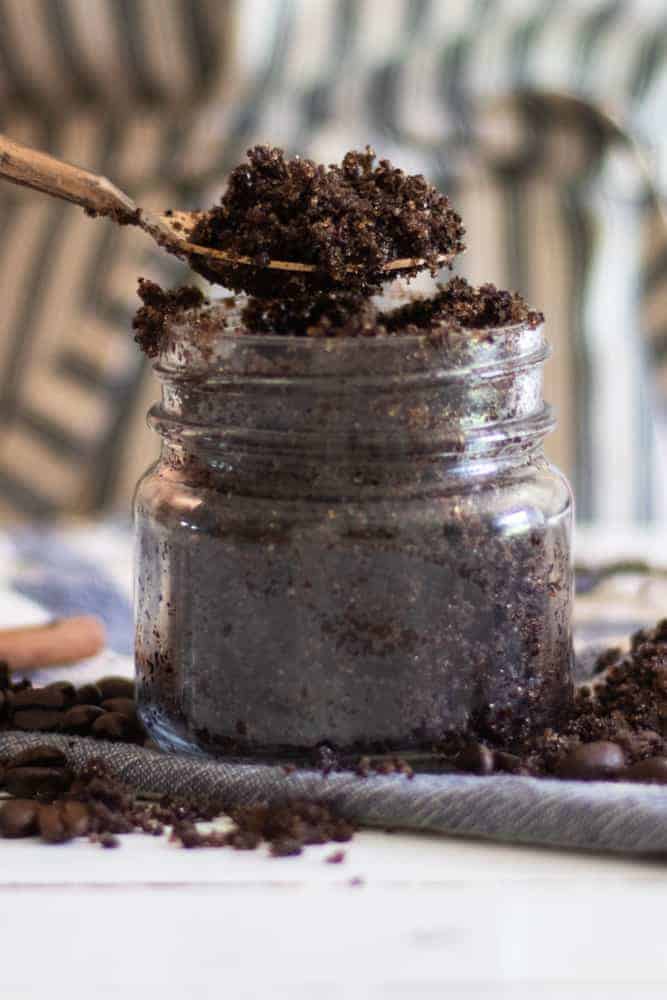 Spooning a DIY coffee body scrub from glass jar.