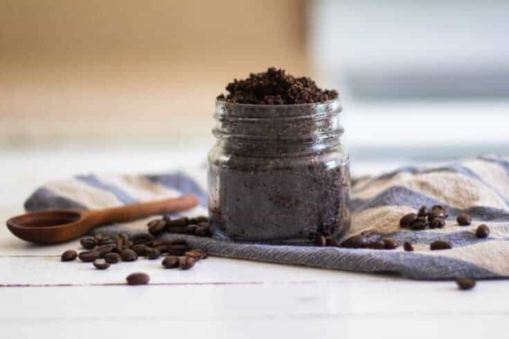 Organic coffee scrub in mason jar with wooden measuring spoon coffee beans and a blue and white striped towel.