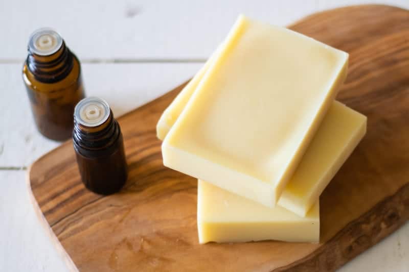 3 conditioner bars on wooden cutting board with 2 empty essential oil bottles.