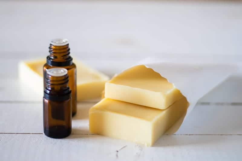 Homemade conditioner bars in white pouch on white shiplap with two amber essential oil bottles.