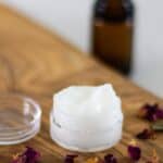 homemade eye cream on wooden board with essential oil bottle in background