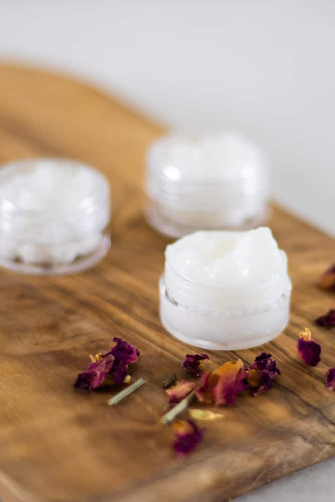 under eye cream in small glass containers on wooden top and dried rose petals