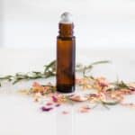 Anti aging rollerball bottle with rose petals on a white marble table.