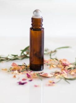 Anti aging rollerball bottle with rose petals on a white marble table.