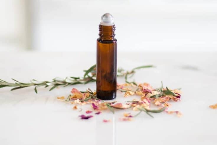 Anti aging rollerball bottle with rose petals on a white marble table.