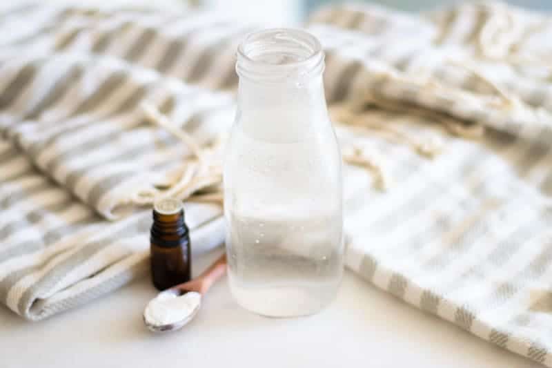 homemade mouthwash in glass container on white marble with striped tea towel behind it