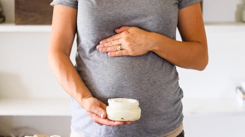 pregnant women holding small glass jar of homemade stretch mark lotion