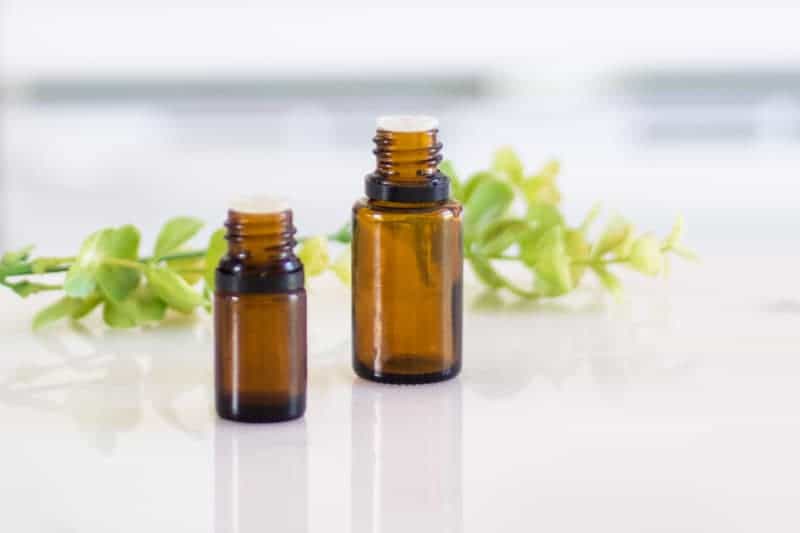 amber essential oil bottles on white marble with green leaf sprigs.