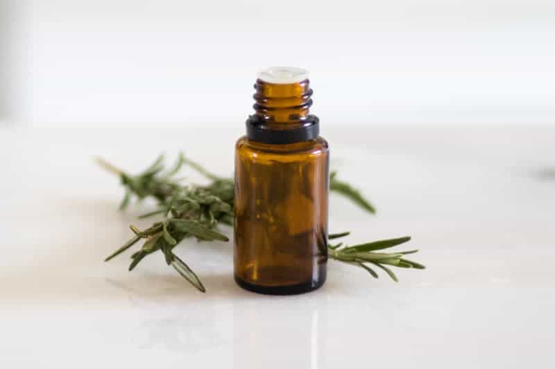 essential oil bottle and fresh rosemary on white marble