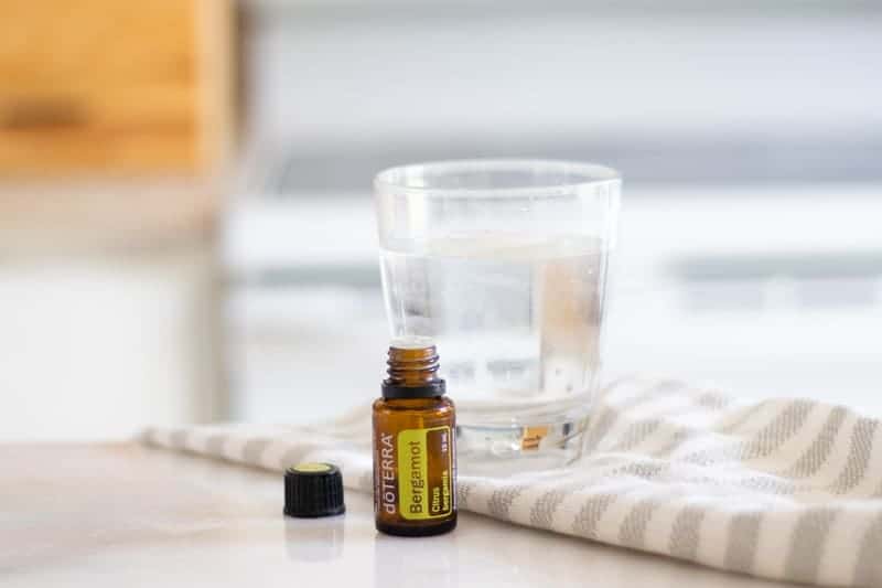 bergamot oil with the lid off in front of glass of a glass of water on a light colored towel