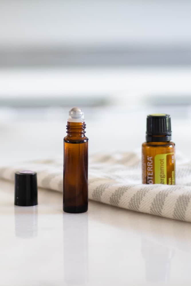 doterra essential oil amber roller bottles on white marble next to grey and white striped towel.