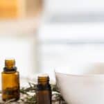 Amber colored essential oil bottles, white bowl, and fresh rosemary on white marble.