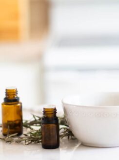 Amber colored essential oil bottles, white bowl, and fresh rosemary on white marble.