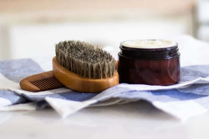 beard conditioner, beard comb, and beard brush on white and blue tea towel