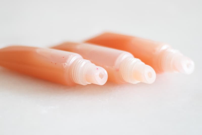 three clear tubes of pink lip gloss 