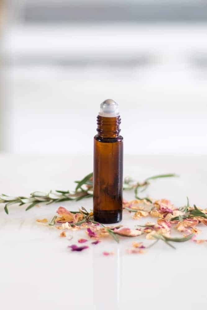 essential oil roller bottle on white marble with floral sprigs on white marble top