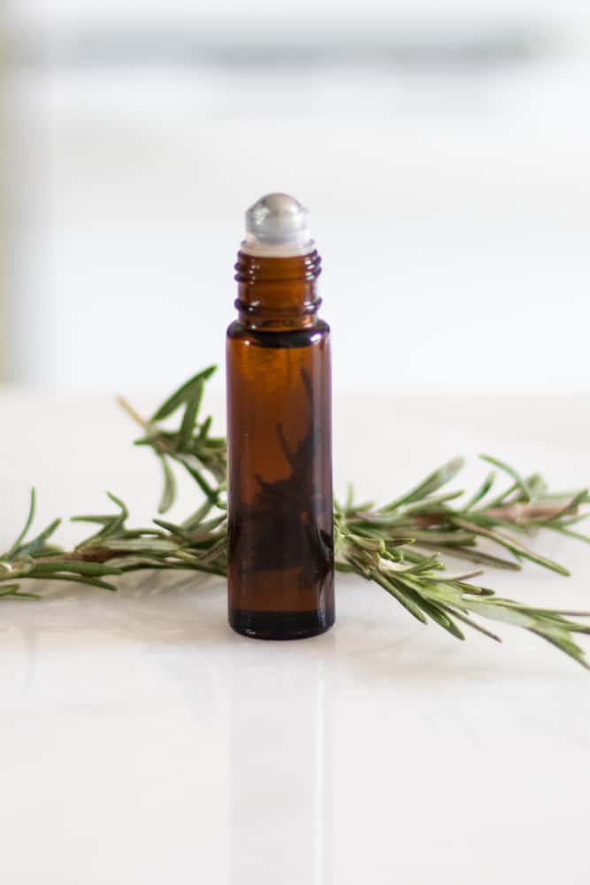 essential oil roller bottle with fresh rosemary behind it