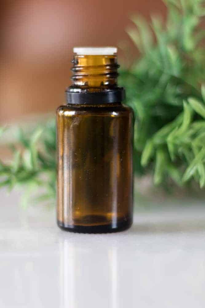 tea tree essential oil bottle with greenery in background on marble counter