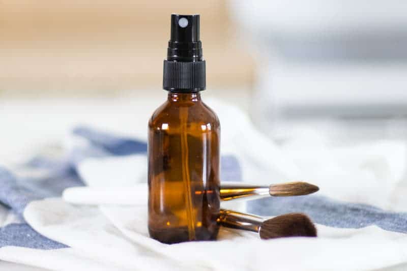 Glass amber colored spray bottle of diy facial toner sitting on white and blue towel.