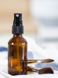 glass spray bottle on white and blue towel with makeup brushes in background