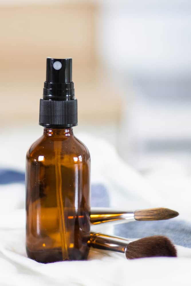 glass spray bottle on white and blue towel with makeup brushes in background