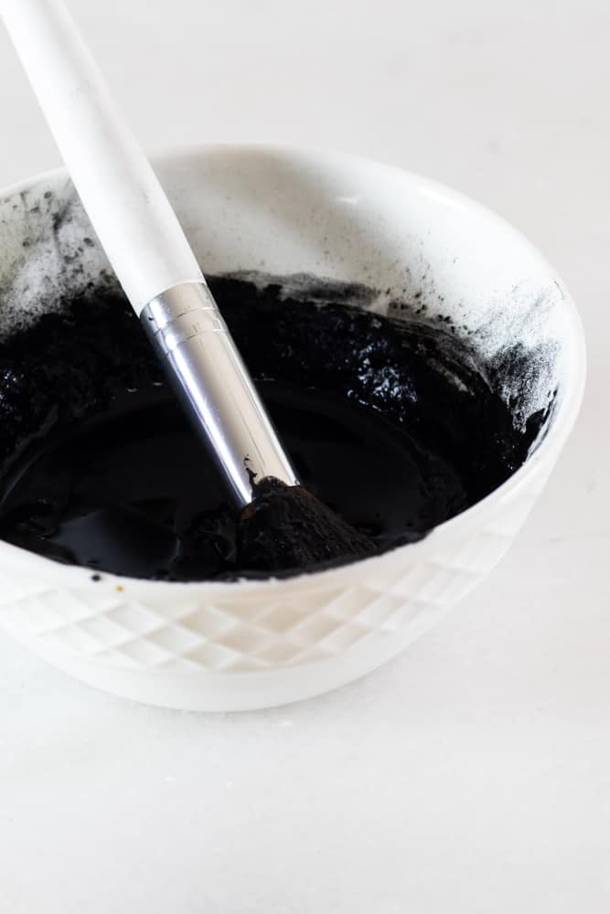 DIY charcoal mask applicator in a small bowl of peel-off mask.