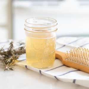 Apple cider hair rinse in mason har with fresh rosemary behind it.
