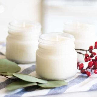 Homemade christmas candles with eucalyptus and cranberries in background.