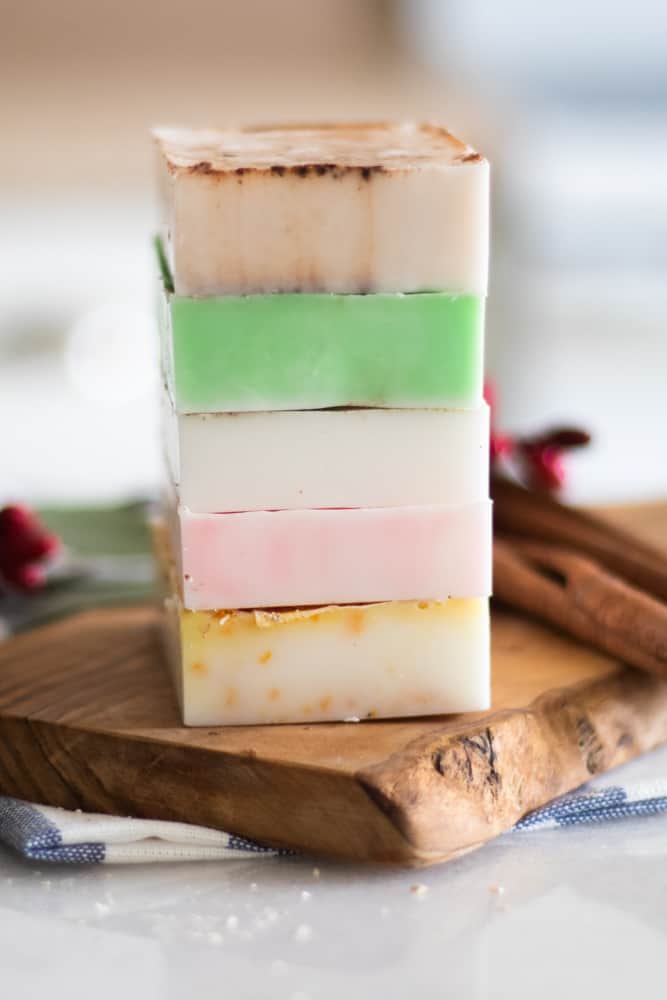 5 melt and pour holiday colored soap bars stacked on wooden tray.